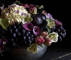 a bowl filled with lots of different types of flowers and fruit on top of a table