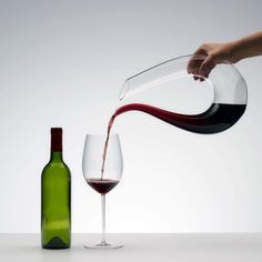 a person pouring red wine into a glass next to a bottle on a white table