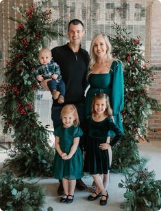 a family posing for a christmas photo in front of an arch with greenery and red berries