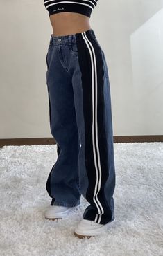 a woman standing on top of a white rug wearing blue jeans and a striped crop top