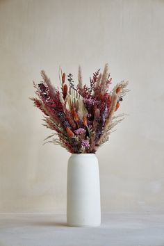 a white vase filled with lots of different types of flowers and plants on top of a table