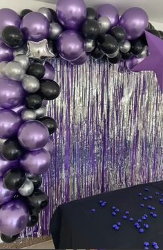 a purple and black balloon arch with streamers on the wall next to a table