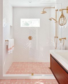 a white bathroom with pink tile and gold fixtures on the shower head, tub, and sink