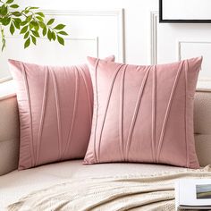 two pink pillows sitting on top of a white couch next to a potted plant