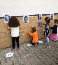 three children are playing with pictures on a bulletin board that is taped to the wall