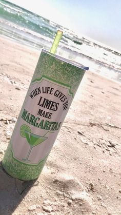 a green and white cup sitting on top of a sandy beach