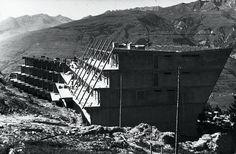 an old black and white photo of a building on top of a hill with mountains in the background