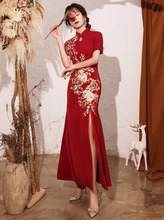 a woman in a red dress standing next to a vase with dried flowers on it