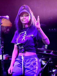 a woman standing in front of a microphone and making the peace sign with her hand