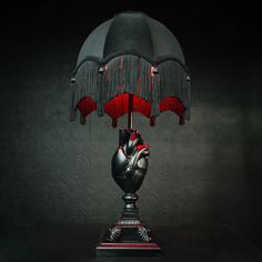 a table lamp with a black and red shade on it's base, in the shape of a human hand