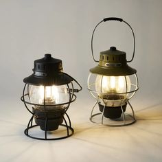 two old fashioned oil lamps sitting side by side on a white surface, one is turned on and the other is off