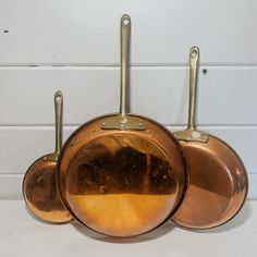 three pots and pans hanging from hooks on a wall