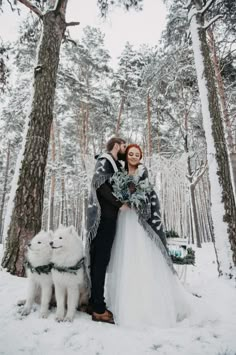 a bride and groom standing in the snow next to their white dog, holding an evergreen wreath