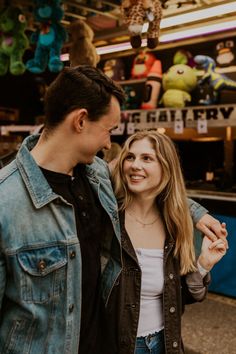 a man and woman standing next to each other in front of a food stand with stuffed animals