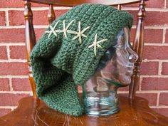 a green knitted hat with white stars on the front and side, sitting on top of a wooden chair