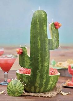 a watermelon cactus sitting on top of a wooden table next to two cocktail glasses