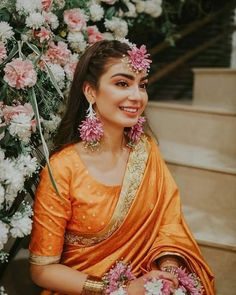 a woman in an orange sari with flowers on her head sitting next to stairs