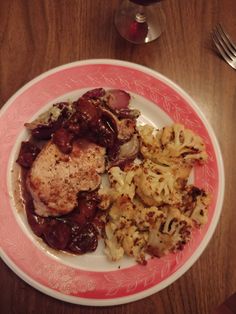 a pink and white plate topped with meat, vegetables and gravy next to a glass of wine