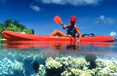 a woman in a red hat is kayaking through the water with corals and trees