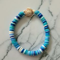 a blue and white beaded bracelet with a sea shell on the clasp, sitting on a marble surface