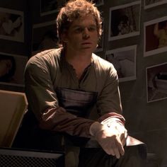 a man sitting on top of a chair in front of a wall with pictures behind him