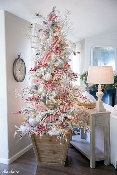 a white christmas tree with red, white and silver decorations in a living room area