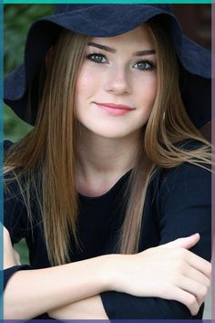 a woman wearing a black hat with her arms crossed and looking at the camera over her shoulder