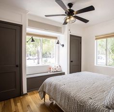 a bedroom with a bed, two windows and a ceiling fan in the middle of it