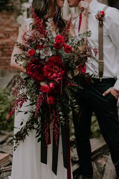 a bride and groom standing next to each other with red flowers in their bouquets