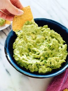 a person dipping guacamole into a bowl with tortilla chips on the side