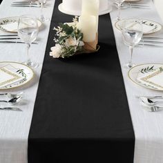 a black table runner with white flowers and candles on it, along with other place settings