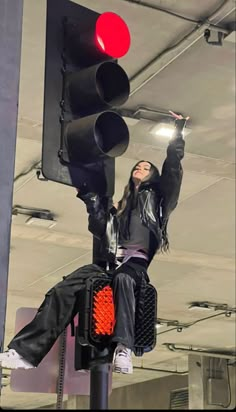 a woman sitting on top of a traffic light with her arms up in the air