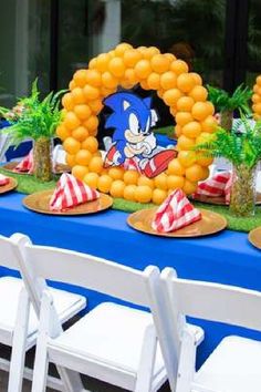 a blue table topped with lots of plates and chairs next to a sonic balloon arch