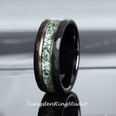 a wedding band with green moss and gold inlays is shown on a black surface