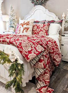 a white bed topped with red and white comforter next to a christmas wreath on top of it