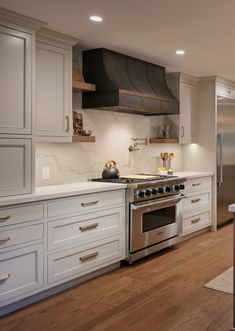 a kitchen with white cabinets and stainless steel stove top oven in the center, along with wooden flooring