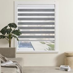 a living room with a couch, chair and large window covered in blinds that look out onto a swimming pool