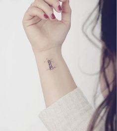 a woman's wrist with a small lighthouse tattoo on the left side of her arm