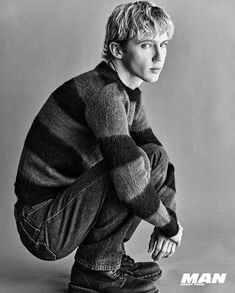 black and white photograph of a man sitting on the ground with his hands in his pockets