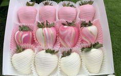 a box filled with pink and white chocolate covered strawberries on top of green grass