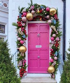 a pink door decorated with ornaments and greenery in front of a white building,