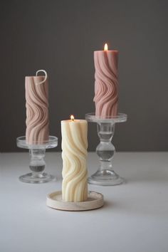 three candles sitting on top of each other next to glass holders with one candle in the middle