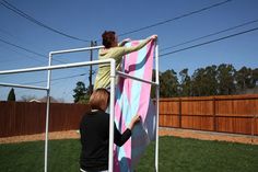 two people standing on top of a pink and blue surfboard in a metal frame