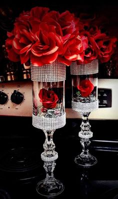 two clear vases with red roses in them sitting on a counter next to an oven