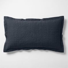 a black pillow on a white wall with a dark blue quilted cover and contrasting pillows