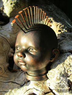 a bronze head statue with hair on it's head sitting next to some rocks