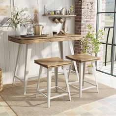 two stools and a table in front of a brick wall with potted plants on it