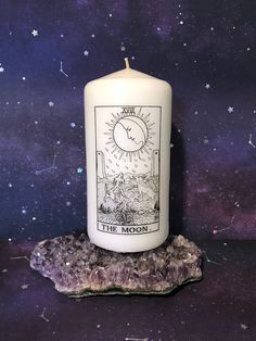 a white candle sitting on top of a rock next to a purple and black background