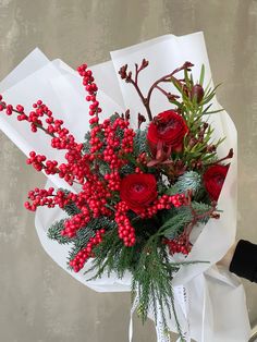 a bouquet of red roses and greenery wrapped in white paper