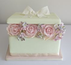 a white cake with pink roses and bows on the top is sitting on a table